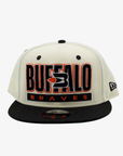 New Era Buffalo Braves cream and black 9FIFTY snapback hat featuring embroidered BUFFALO lettering, retro Braves logo, orange accents, and black flat visor.