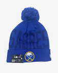 New Era Women's Buffalo Sabres royal blue pom knit hat featuring shimmering SABRES lettering, embroidered crossed-swords logo, and matching blue pom.