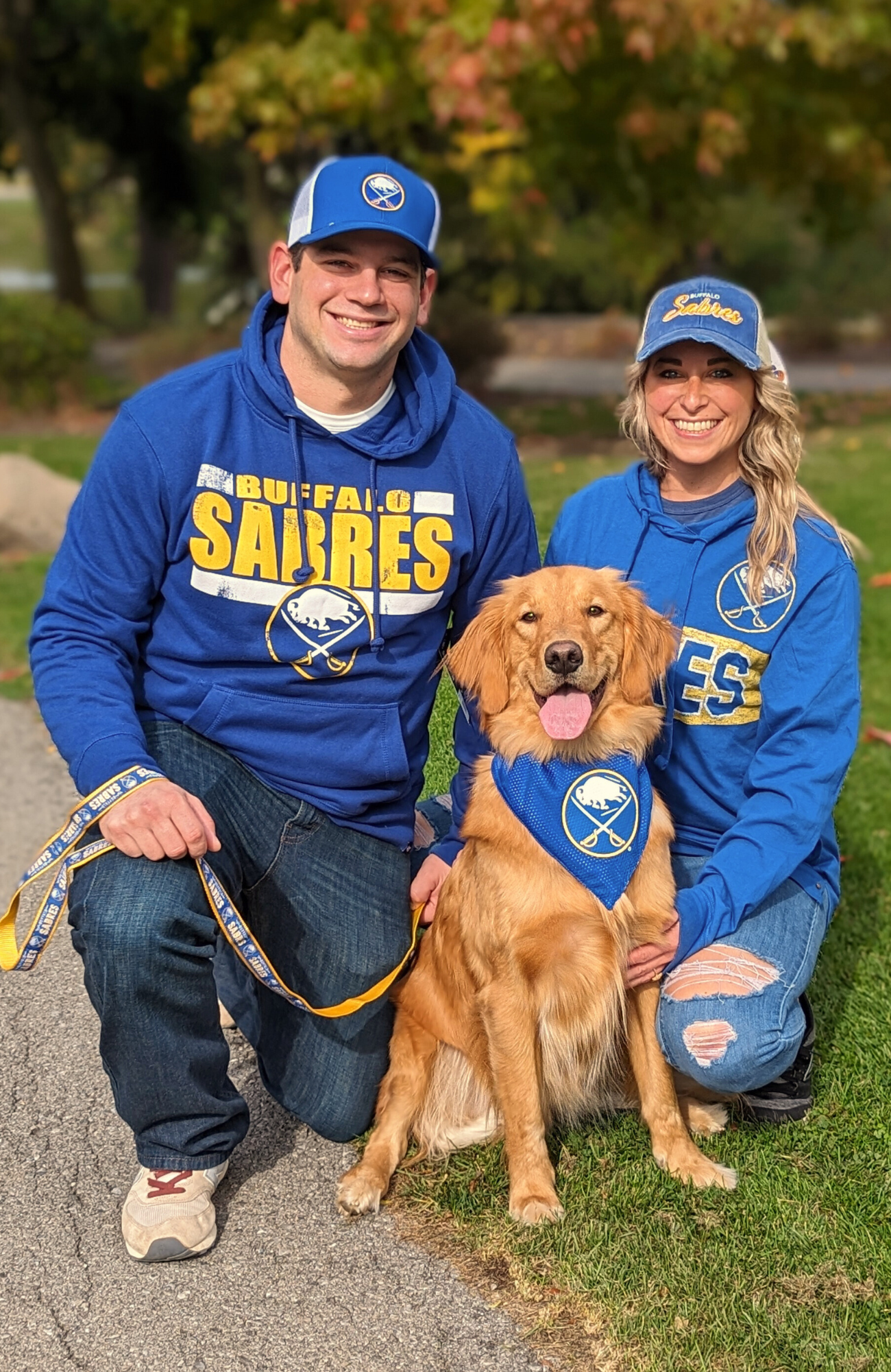 man, woman, and dog posing for picture in a park wearing buffalo sabres clothing