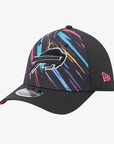 A black baseball cap featuring the Buffalo Bills charging buffalo logo on the front, decorated with vibrant pink, blue, and orange paint-stroke patterns on the front panels. The cap has a black curved brim with a silver reflective sticker on the underside, and a pink New Era logo on the side.