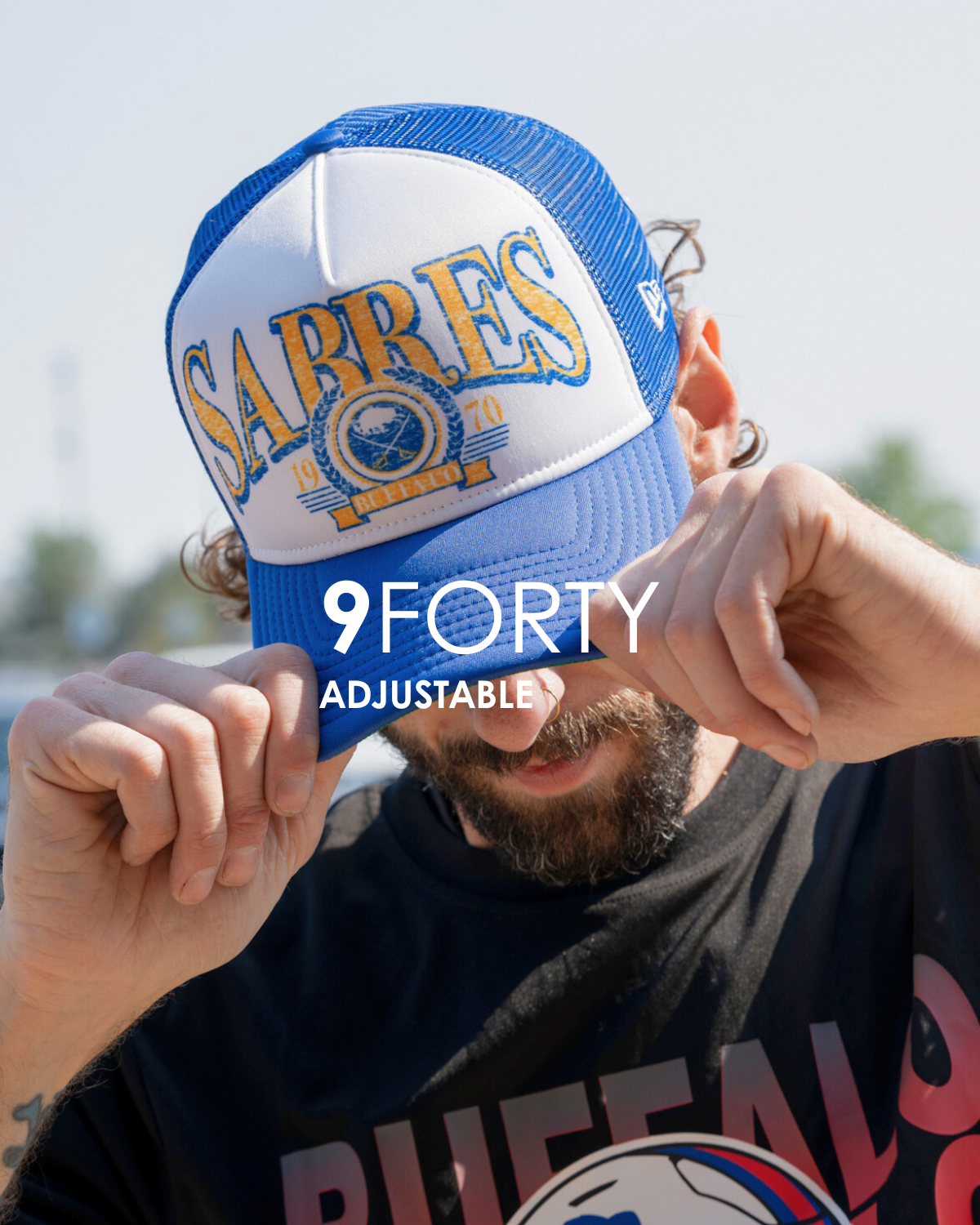 Person wearing a blue and white cap with 'Sabres' branding, held by hands against a blurred outdoor background that is titled 9forty adjustable.