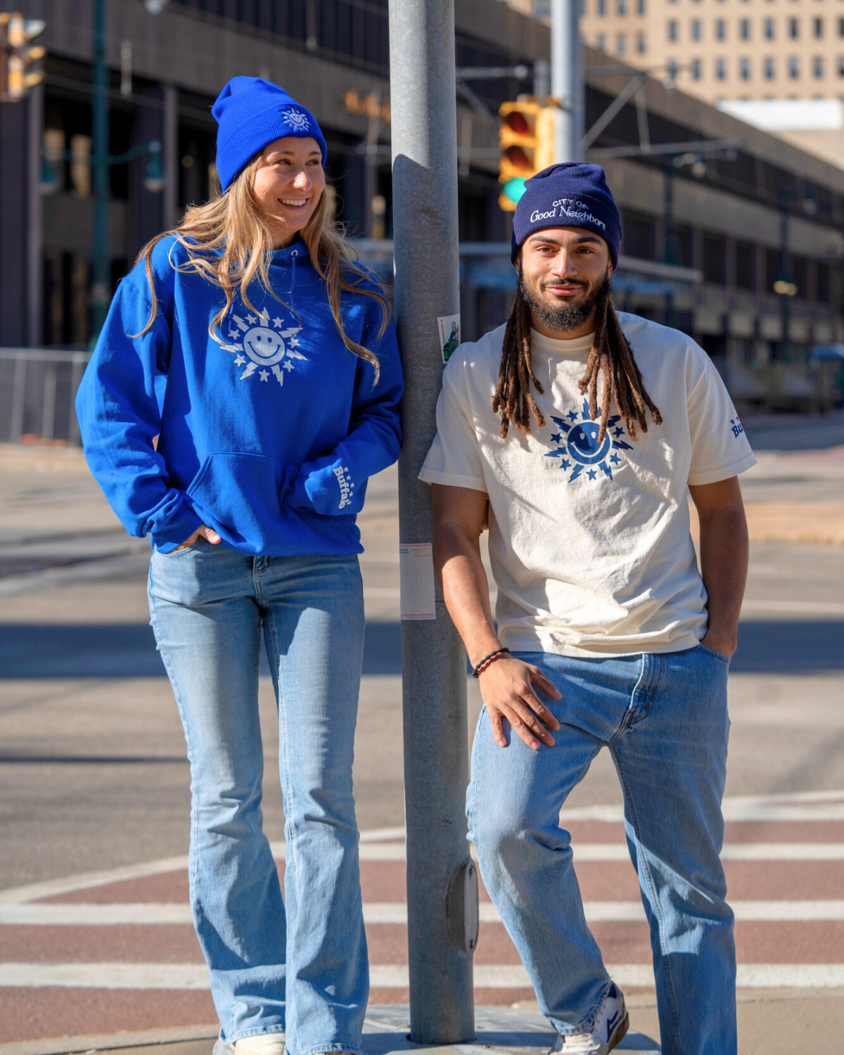 Two people wearing blue and white clothing with logos, standing on a city street.