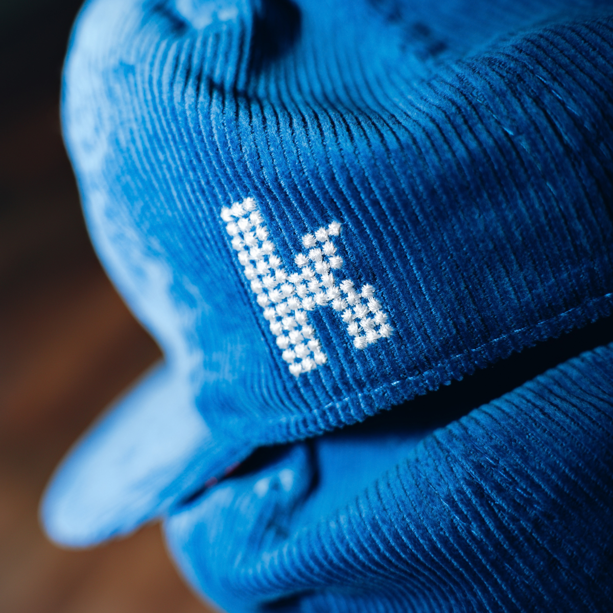 Close-up of white embroidered The Killers K emblem on royal blue corduroy snapback hat