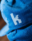 Close-up of white embroidered The Killers K emblem on royal blue corduroy snapback hat