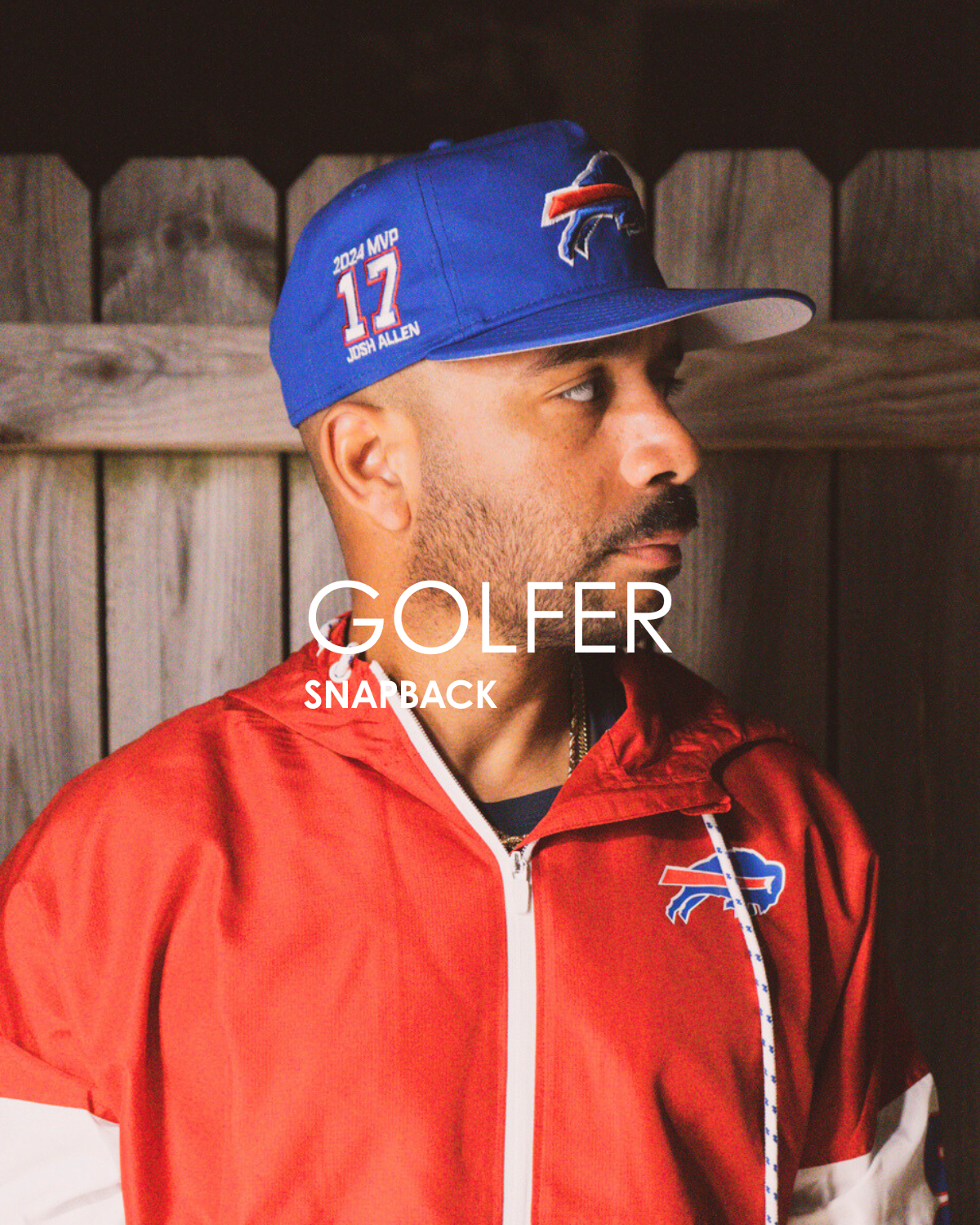 Man wearing a blue cap with a logo and red jacket, standing against a wooden fence that is titled golfer snapback.