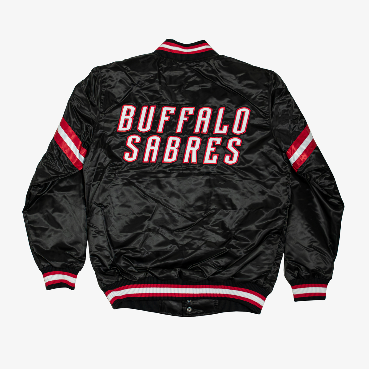 Back view of Starter Buffalo Sabres black satin varsity jacket featuring large white BUFFALO SABRES lettering outlined in red and black, striped sleeves, and matching rib-knit trim.