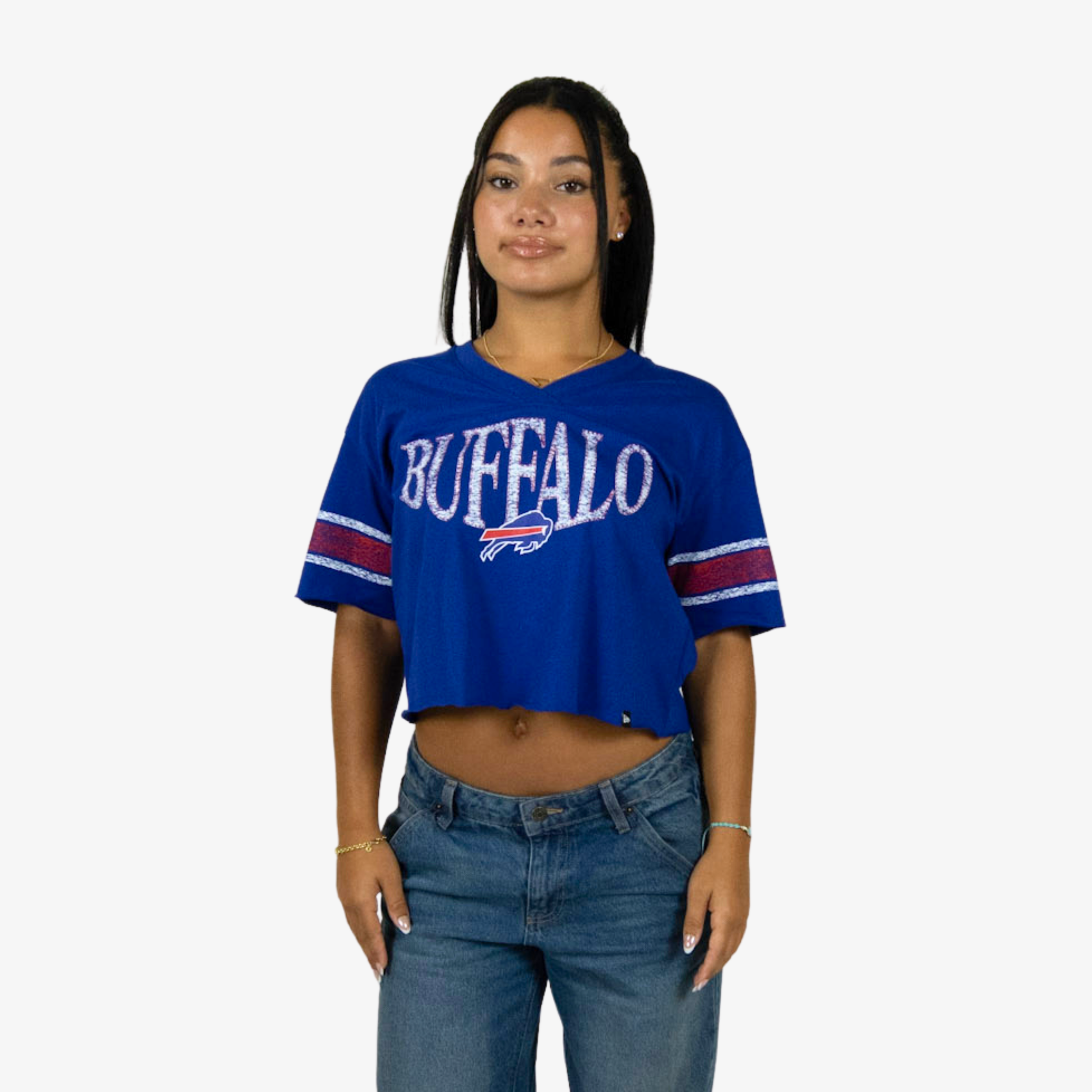 A woman modeling a blue Buffalo Bills cropped t-shirt with 'BUFFALO' and the charging buffalo logo printed on the front, paired with blue jeans against a light gray background.