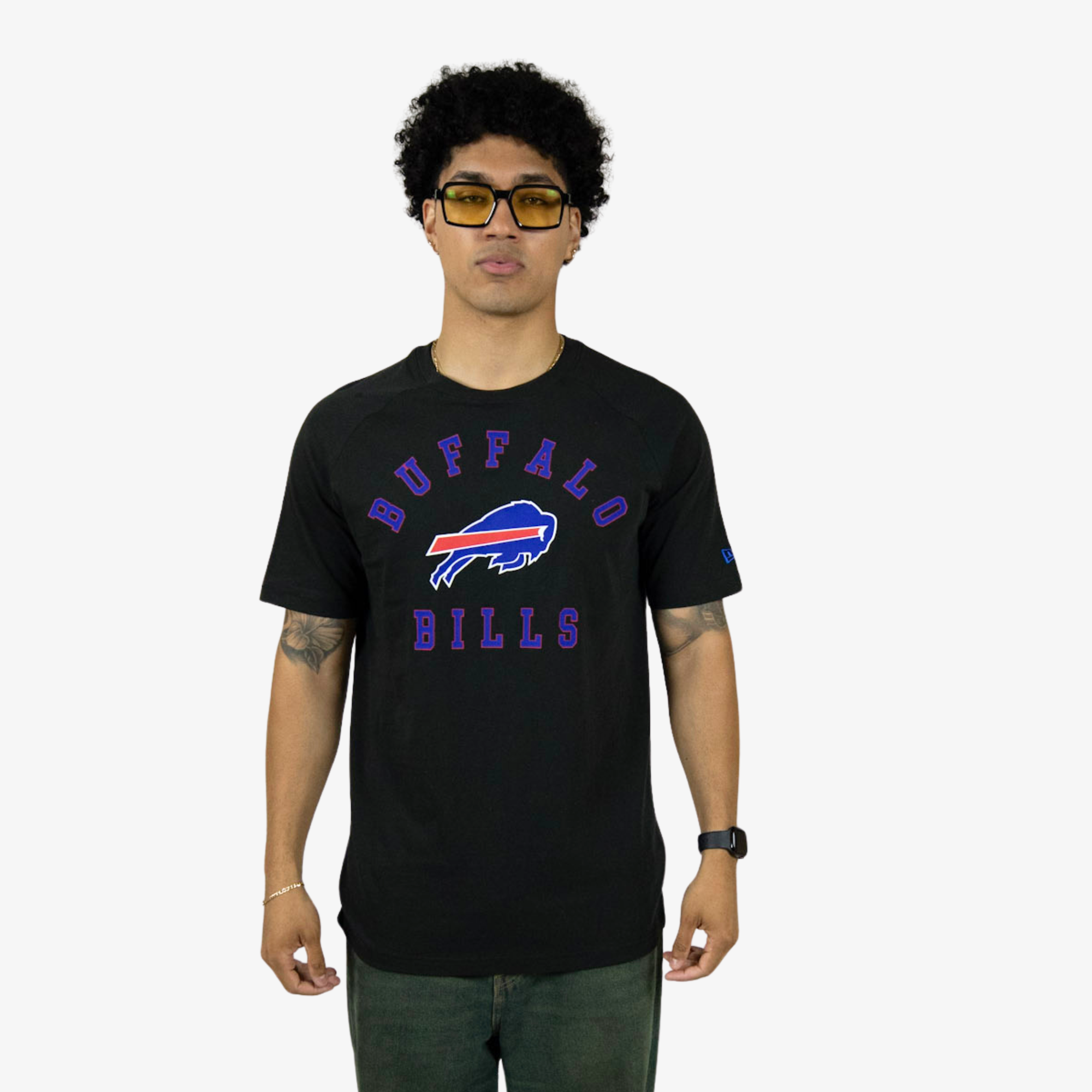 A man wearing a black Buffalo Bills t-shirt with a purple and red graphic logo on the front, paired with dark green jeans, standing against a light gray background.