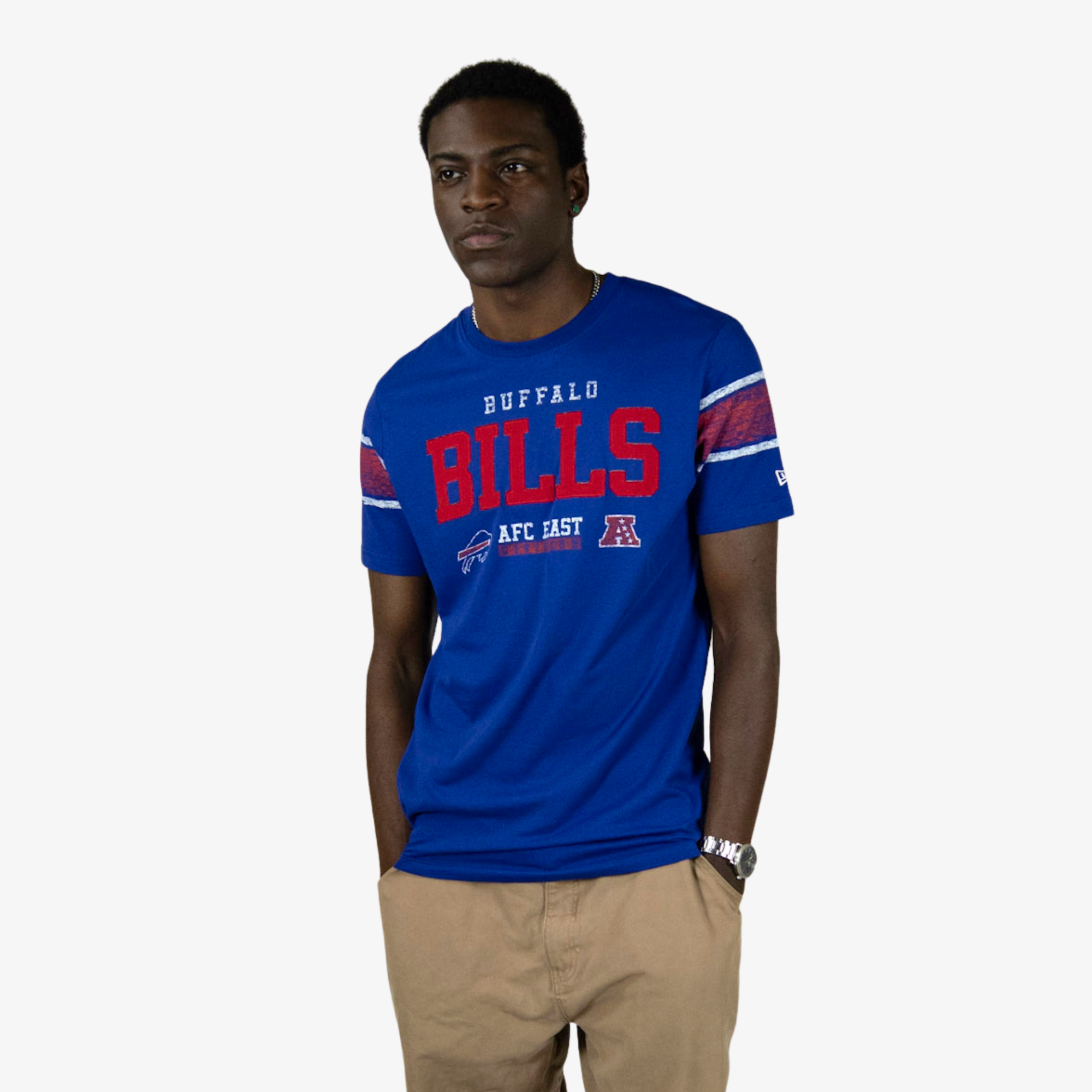 A man wearing a royal blue Buffalo Bills AFC East t-shirt with red and white lettering, paired with khaki pants, standing against a light gray background.