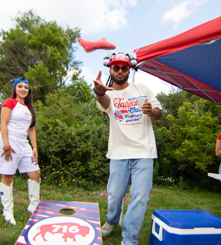 man playing corn hole while wearing buffalo tailgate club tshirt