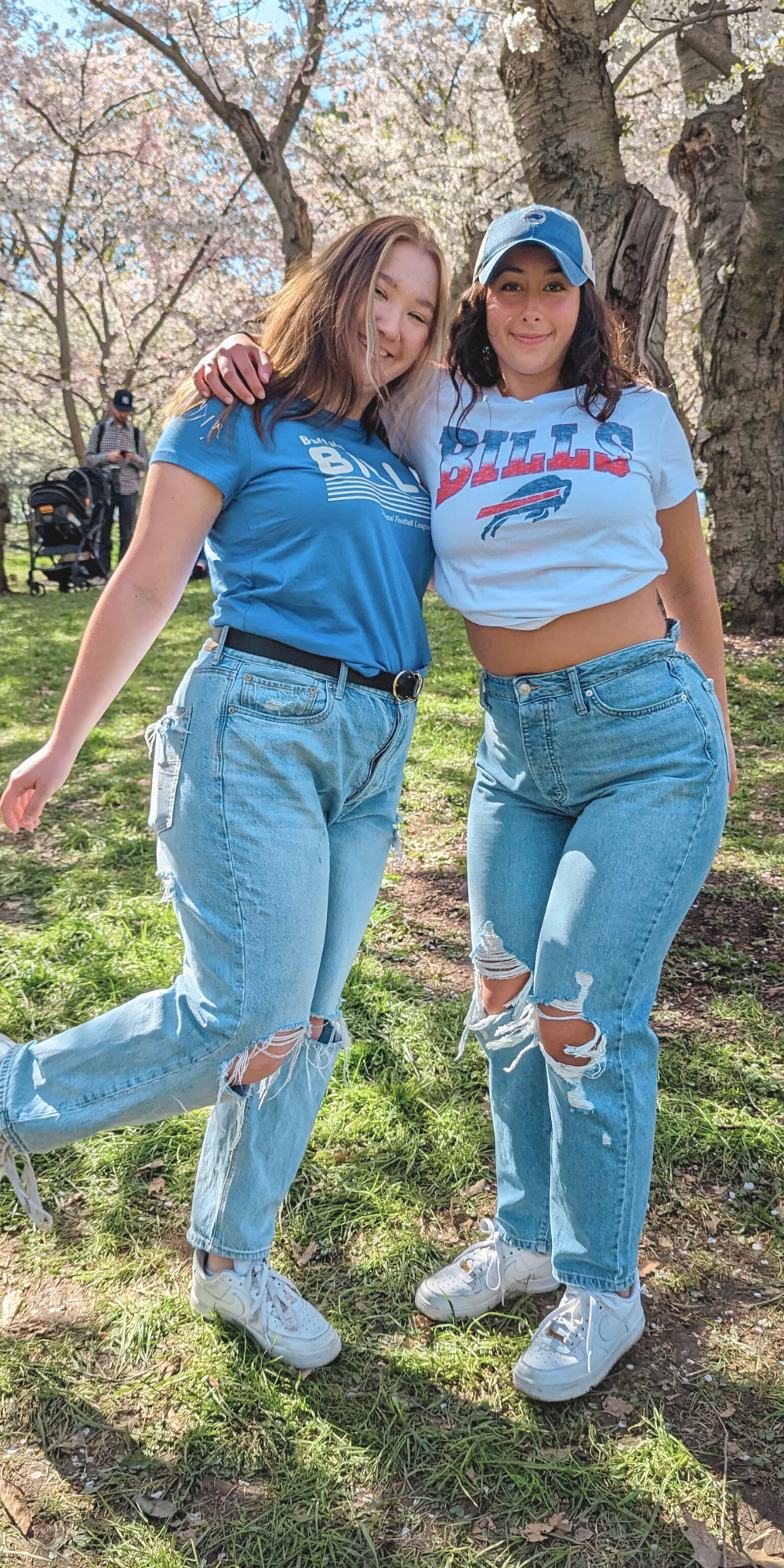 two women posing for a picture. one wearing a light blue buffalo bills short sleeve shirt and the other wearing a white buffalo bills short sleeve shirt