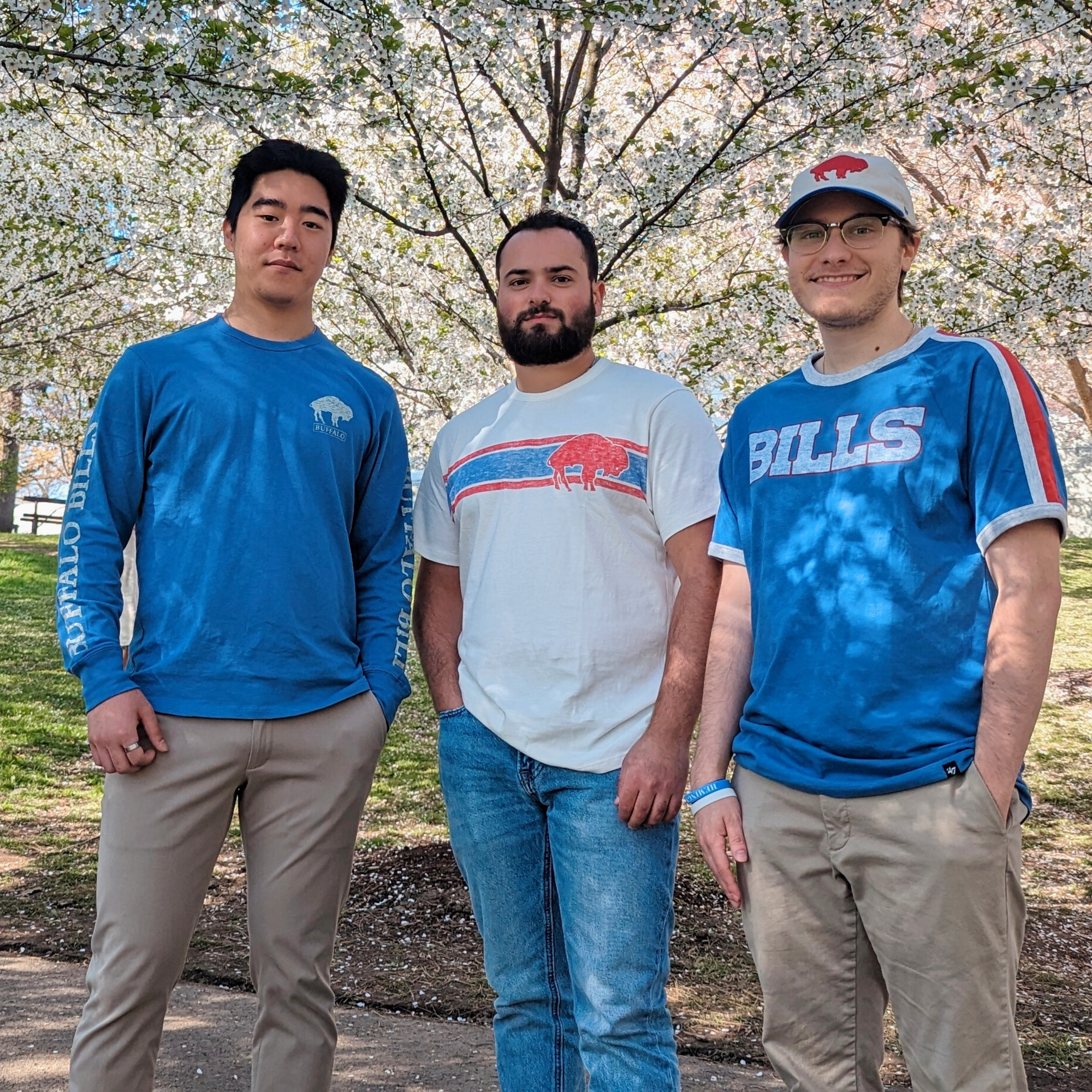 Three men posing for a photo in the park. they are all wearing buffalo bills shirts