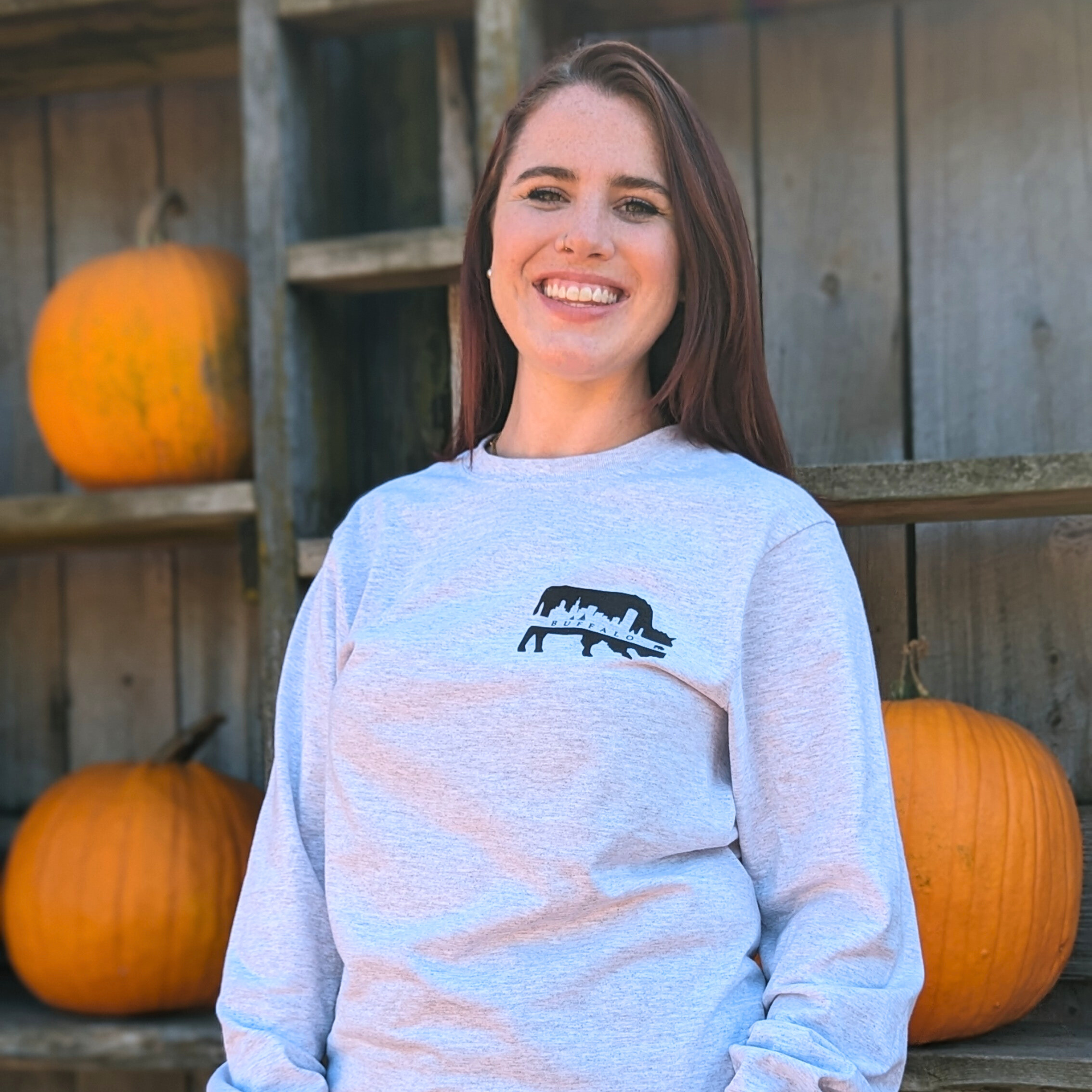 woman posing for a photo wearing a gray buffalo themed long sleeve shirt at a pumpkin patch
