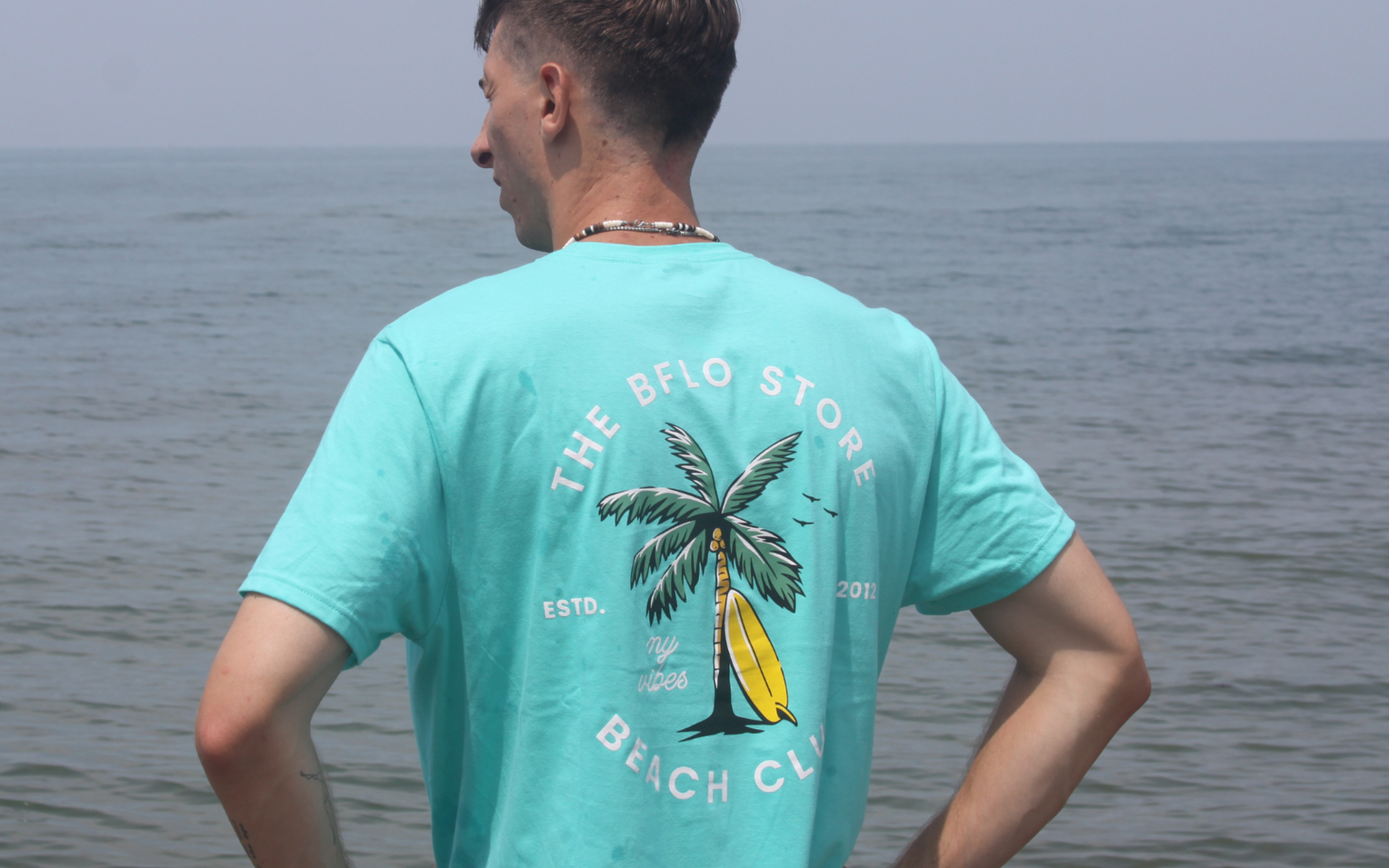 man at the beach wearing an aqua bflo beach club tshirt